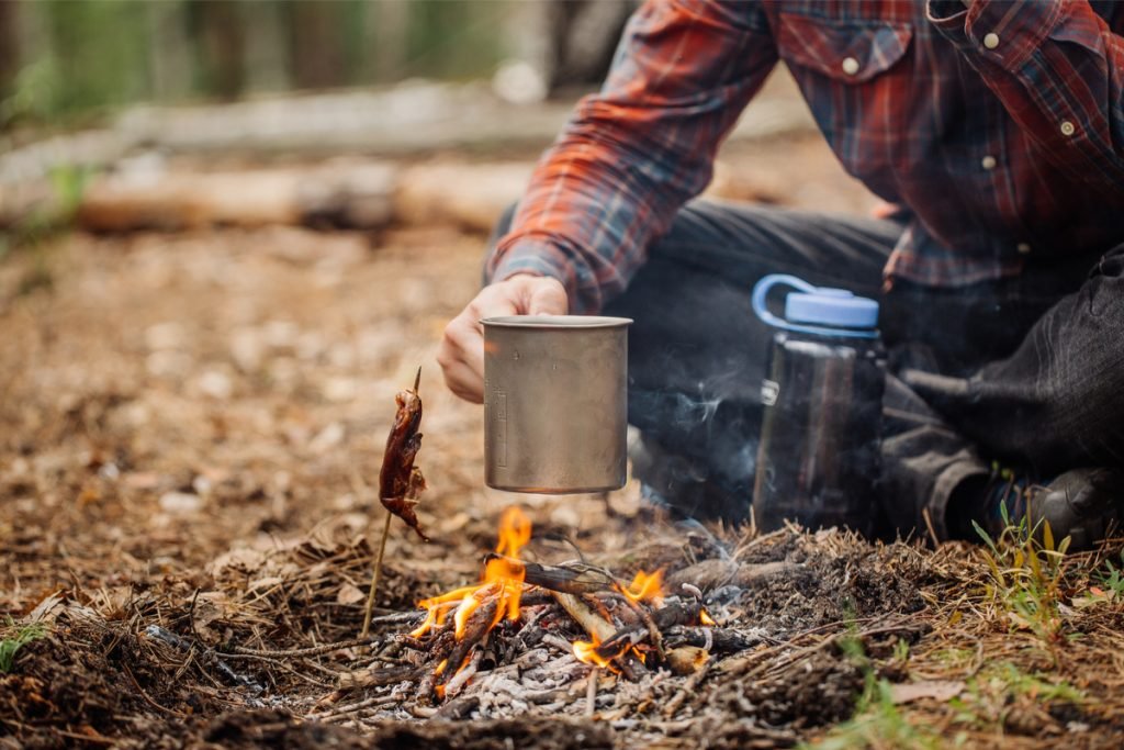 Making coffee in mug over small campfire