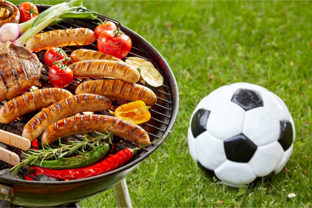 Barbeque grill laden with food.  Soccer ball sitting on ground