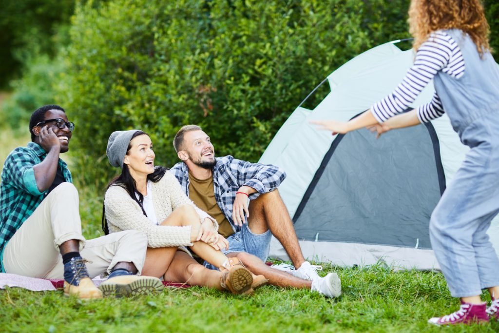 4 adults playing charades in front of a tent
