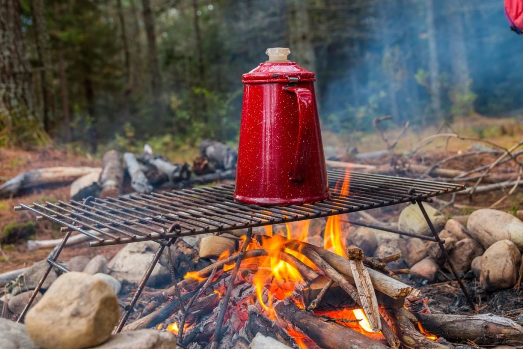 Red coffee pot on a grill rack over an open campfire.  This is the traditional way to make great coffee while camping