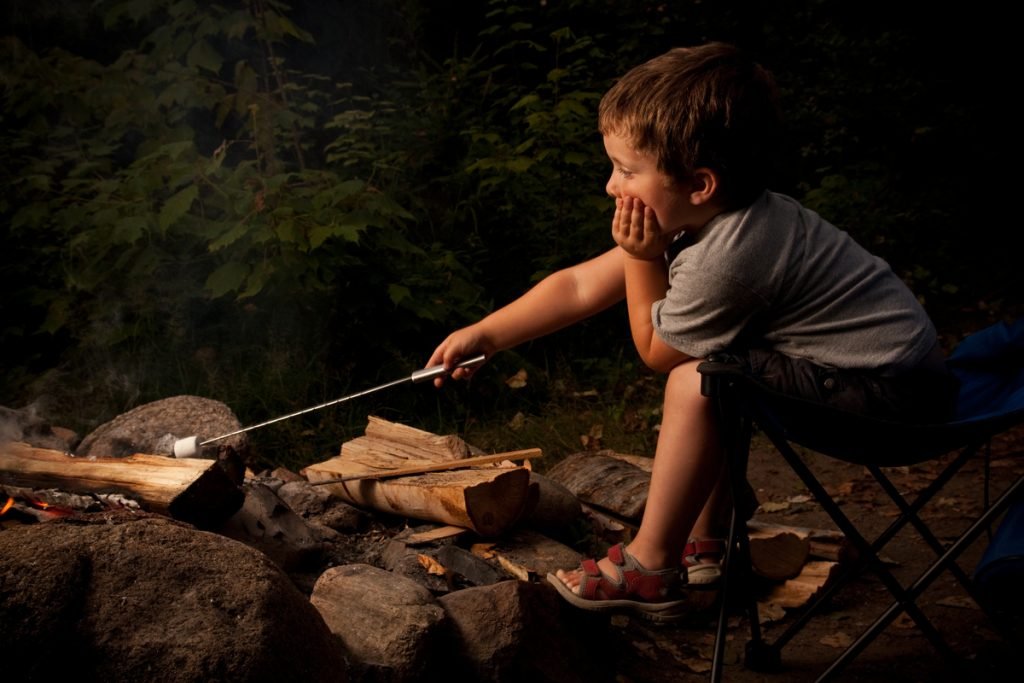 Young boy trying to roast a marchmallow over small campfire