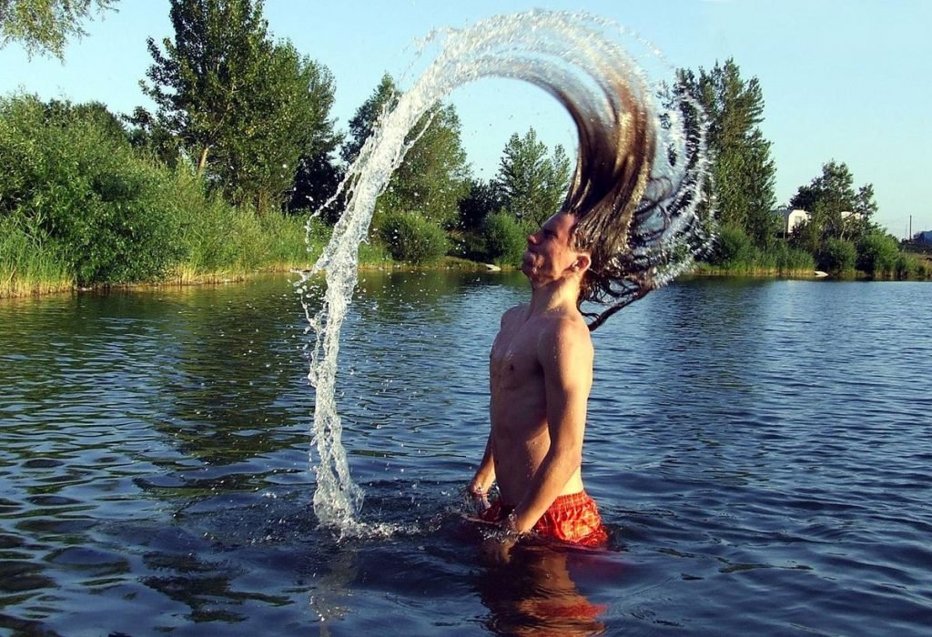 Man with long hair removing excess water while in lake
