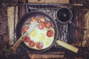 Eggs and Tomatoes cooking in a frying pan over a campfire