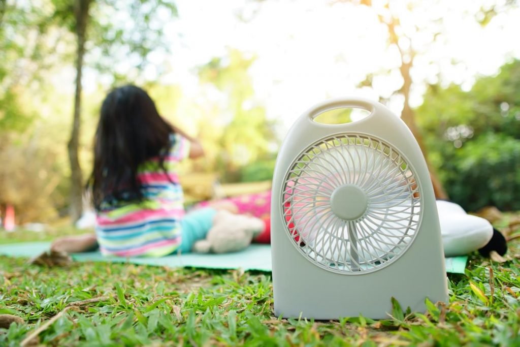 Family camping tent fan in foreground, youg girl on picnic blanket behind